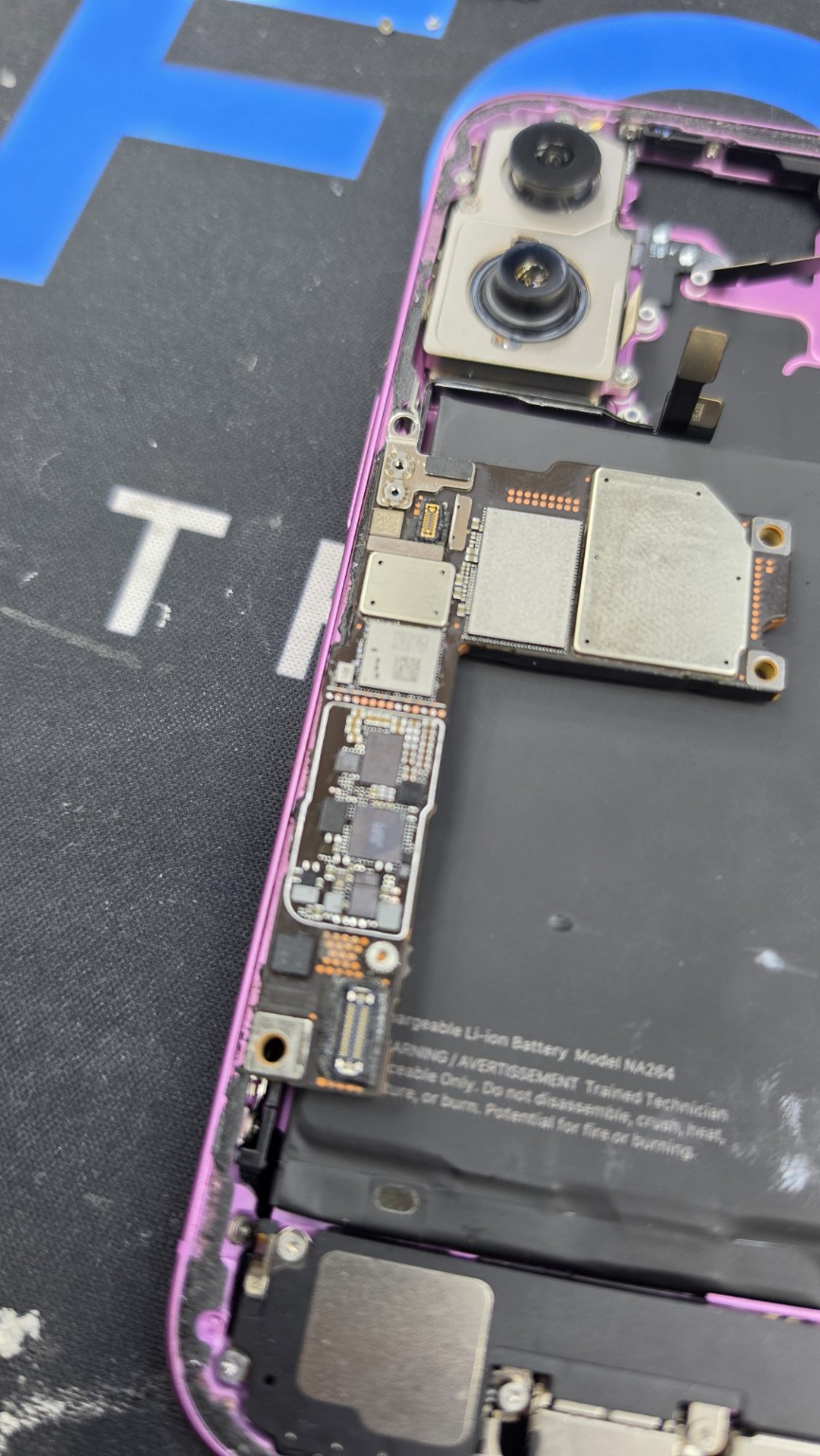 Motherboard resting inside the opened pink iPhone 16 alongside its cameras and battery